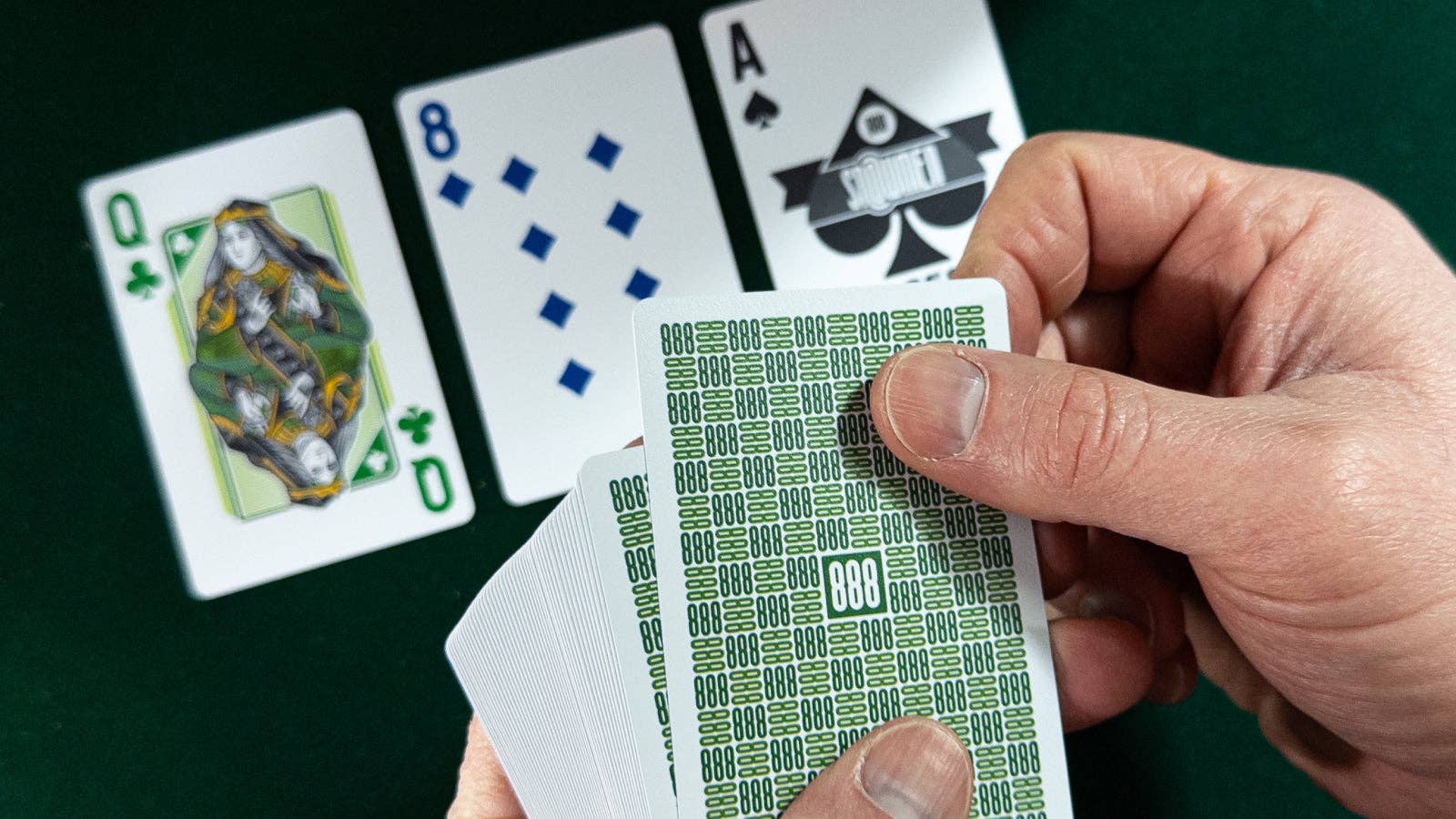 Hand holding a deck of cards with visible card faces on a green surface