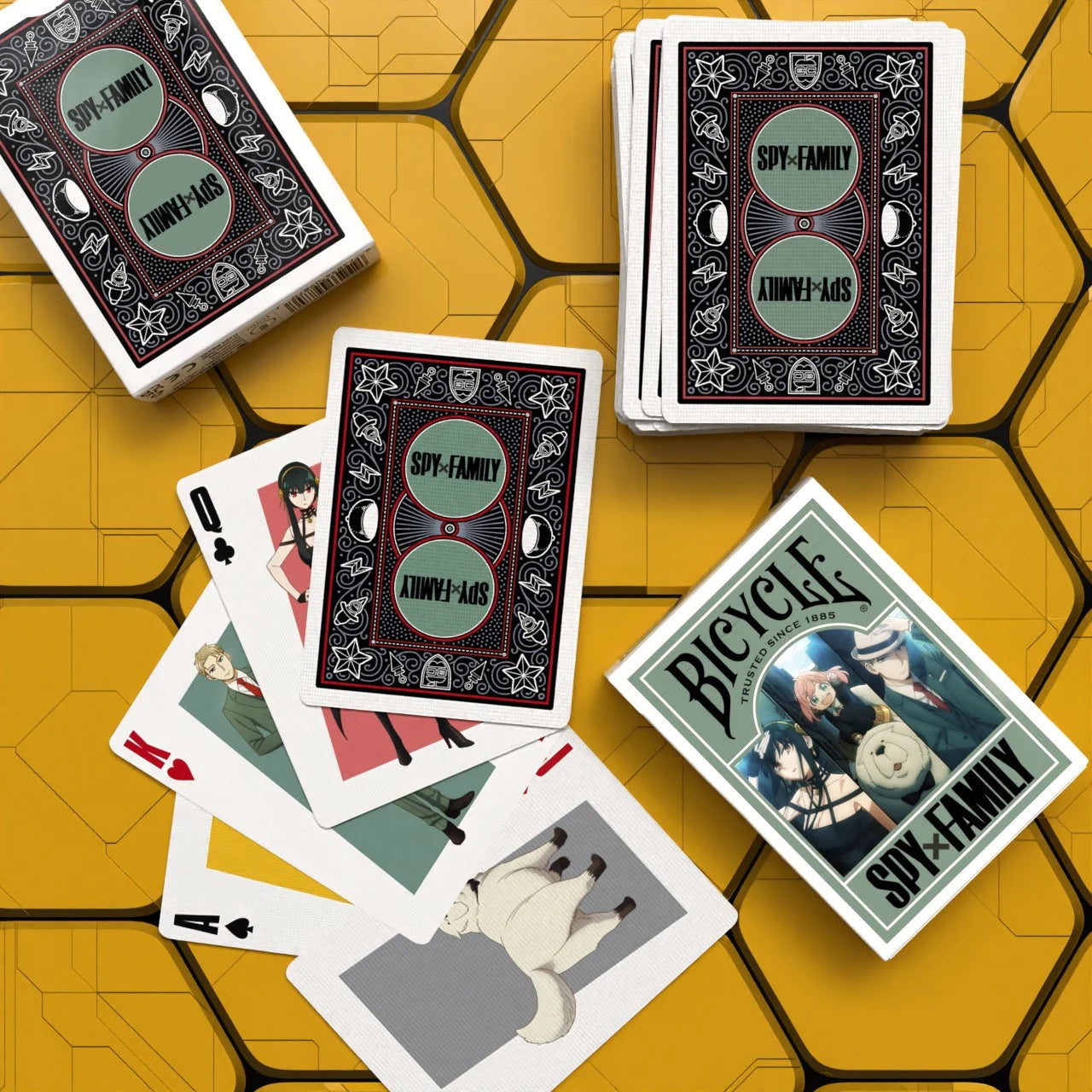 Stacks of Bicycle Spy x Family cards on yellow table with custom backs and character cards fanned in the foreground.