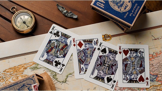 Four playing cards (King of Clubs, King of Diamonds, King of Spades, King of Hearts) on a map with a pocket watch and card box in the background.