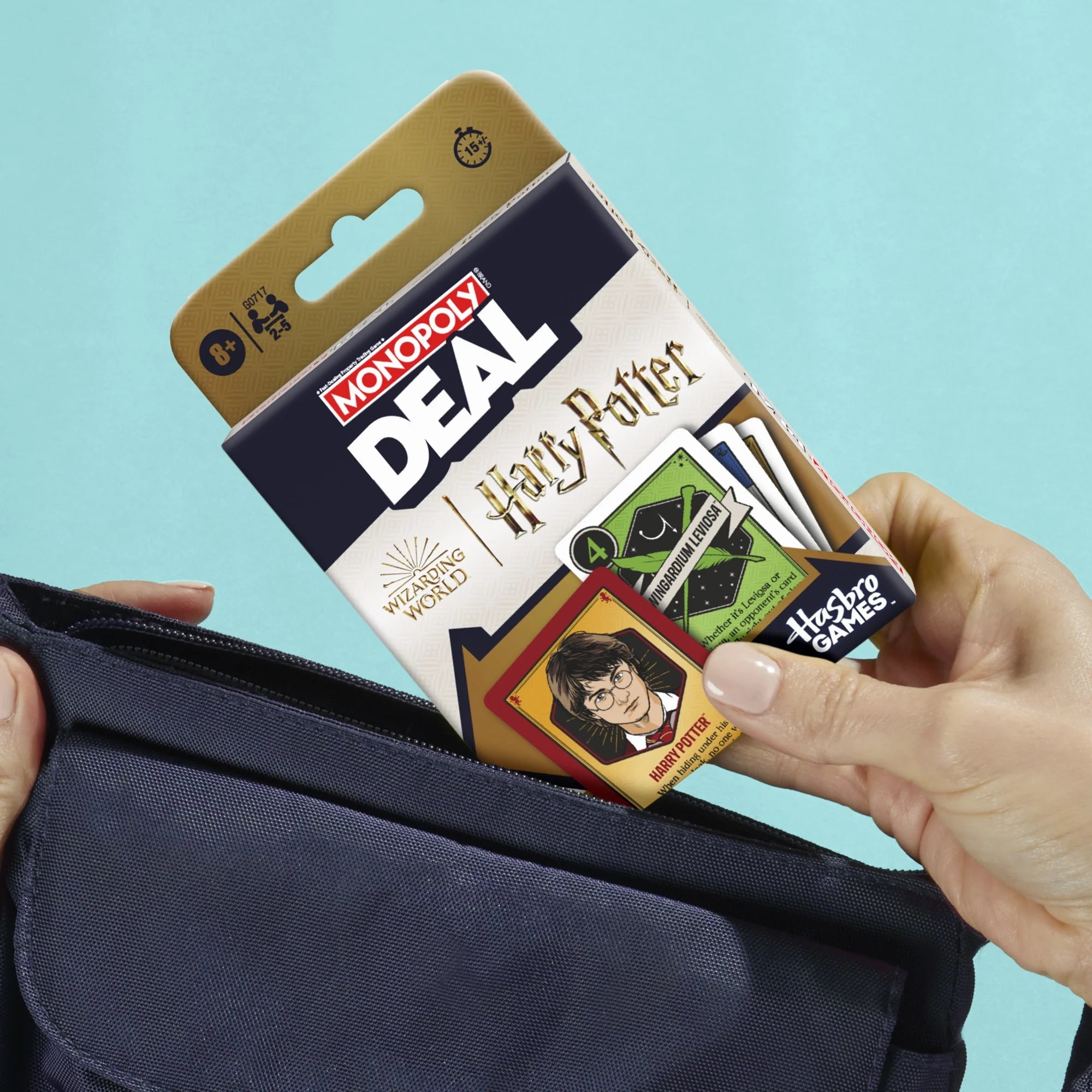 Hand holding a Monopoly Deal Harry Potter card game packaging against a teal background