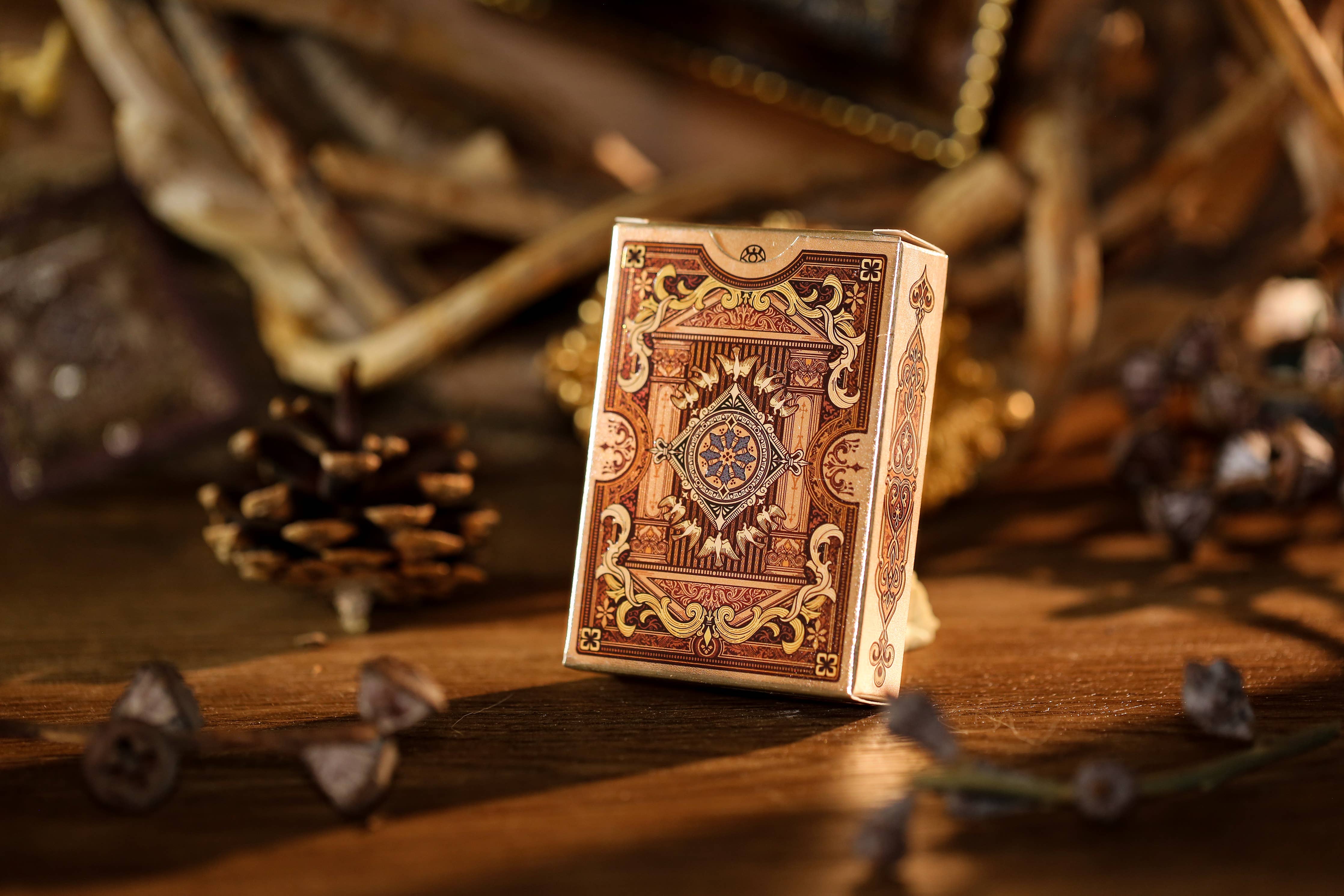 Decorative playing card box on a wooden surface with pine cones and branches.
