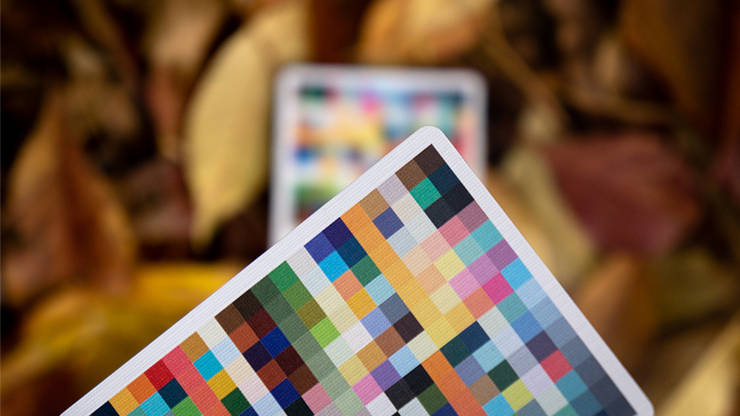 Color swatch card held in front of a blurred tablet displaying a colorful screen.