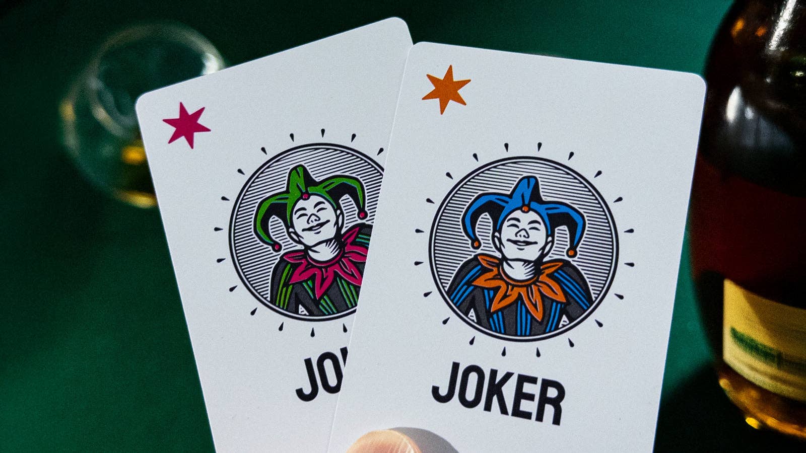 Two playing cards featuring Vanda Aces 2.0 Jokers on a green background with a bottle.