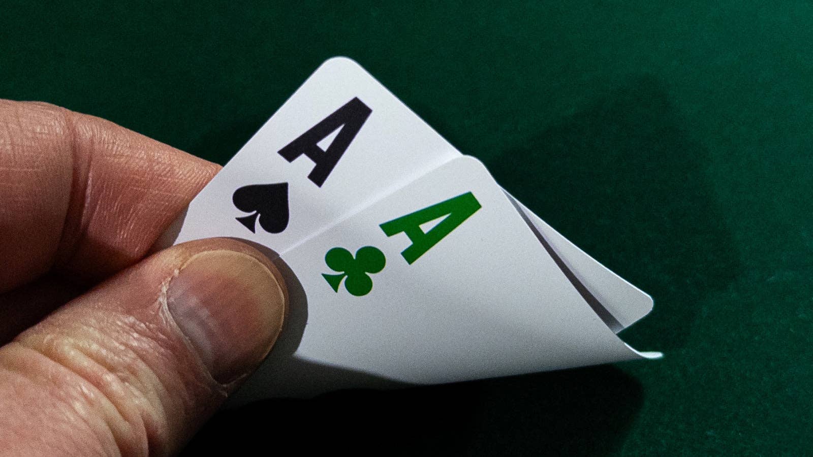 Two Vanda Aces 2.0 playing cards, including an Ace of Spades and Aces of Clubs, held by a hand against a green background.