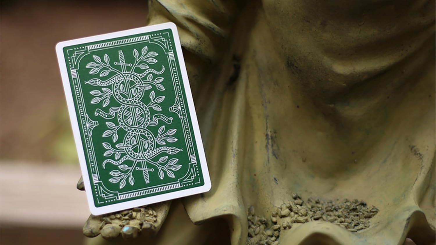 Green playing card with white design held by a statue