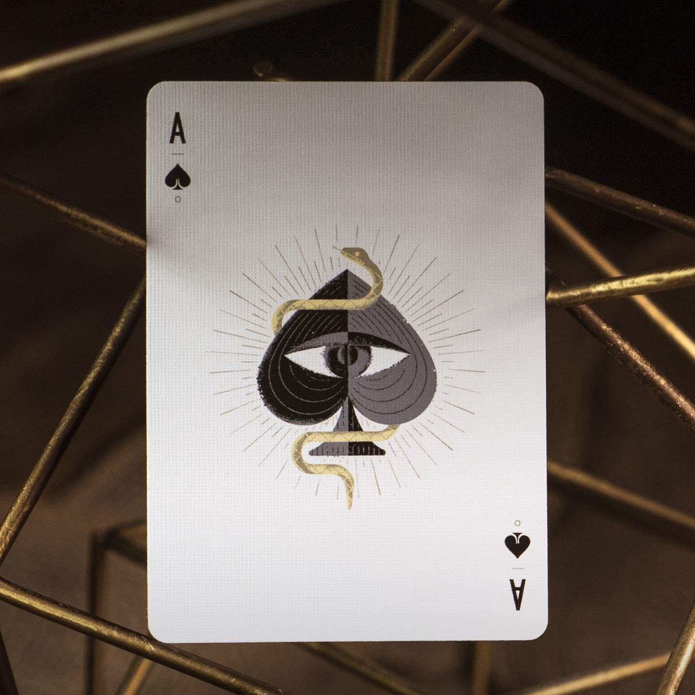 Playing card with ace of spades design featuring a snake and eye symbol on a metallic background.