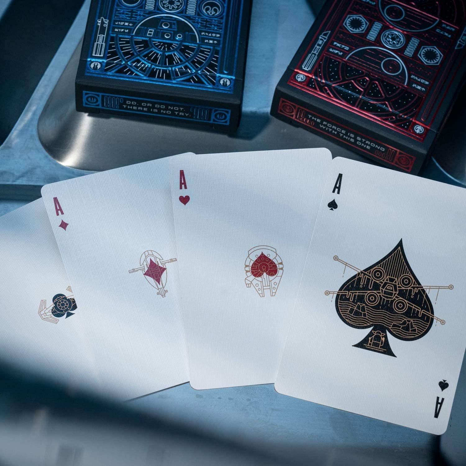 Four aces from a unique playing card set on a reflective surface with two decks in the background.