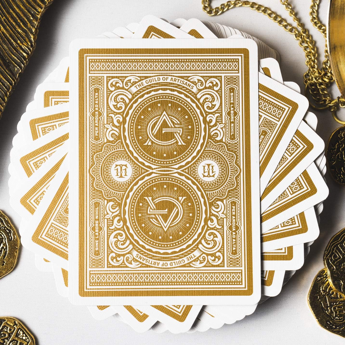 Gold playing cards with intricate designs on a white surface with coins and a chain.