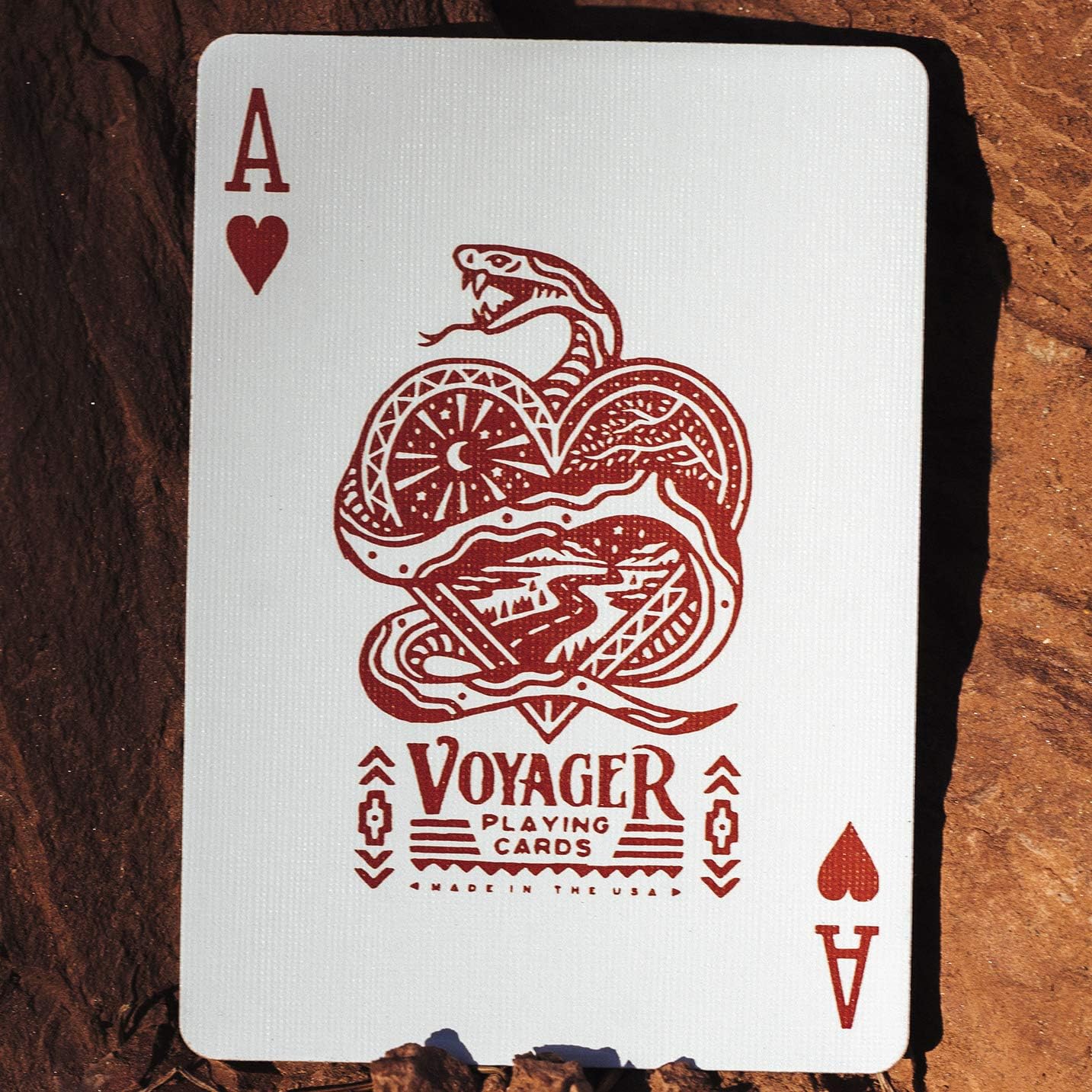 Ace of hearts playing card with a snake design and 'Voyager Playing Cards' text on a wooden surface.