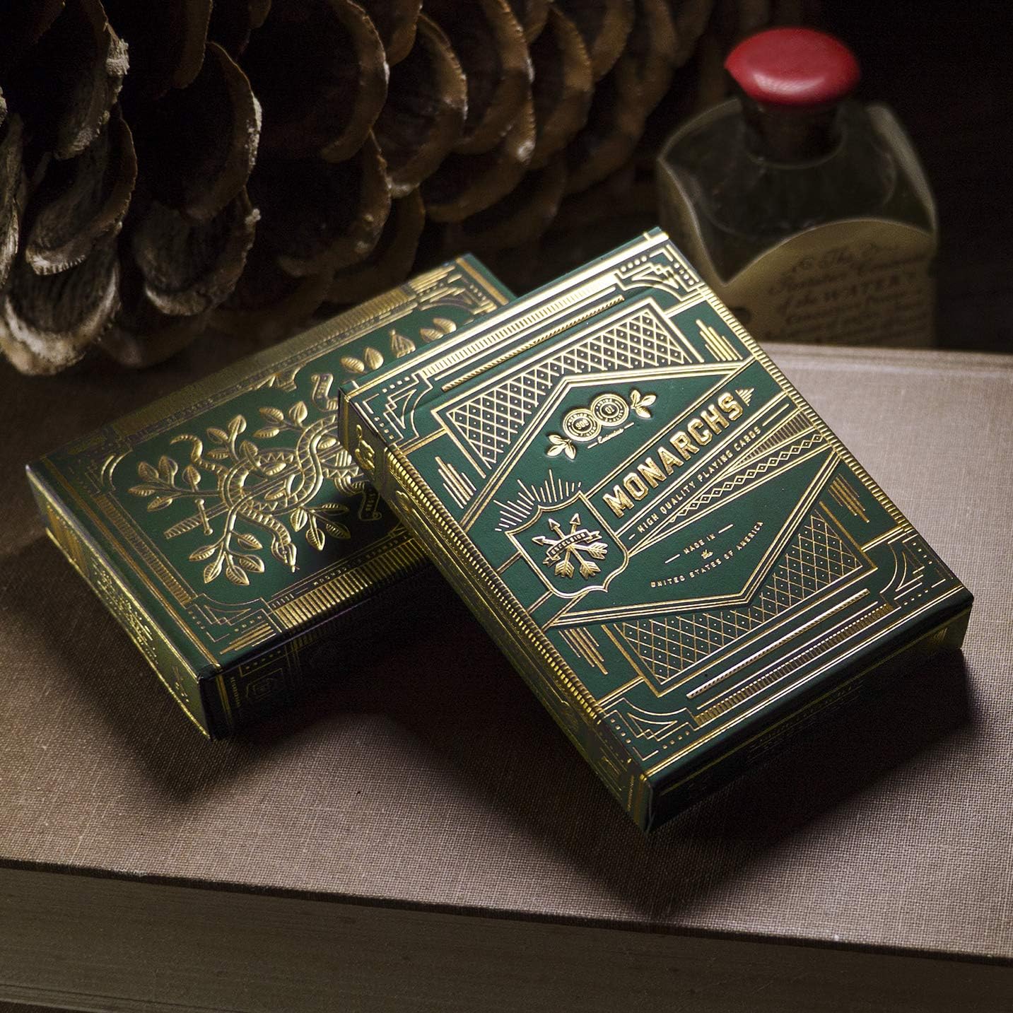 Two Monarch green and gold playing card boxes on a wooden surface with a bottle in the background.