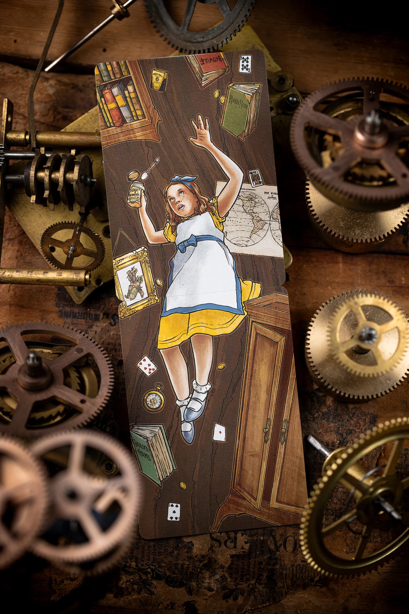 Card featuring a character in a yellow dress surrounded by books and gears on a wooden surface.