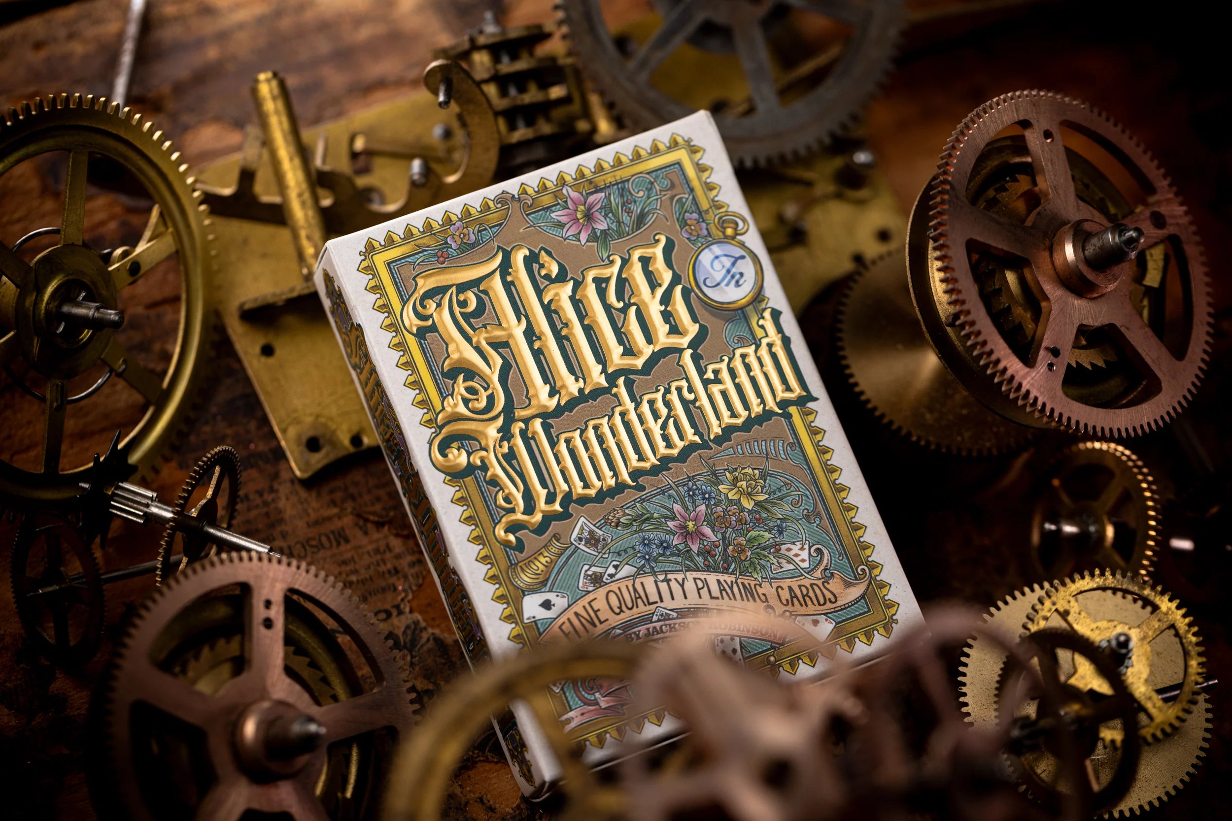 Playing cards with 'Alice in Wonderland' design surrounded by mechanical gears on a wooden surface.