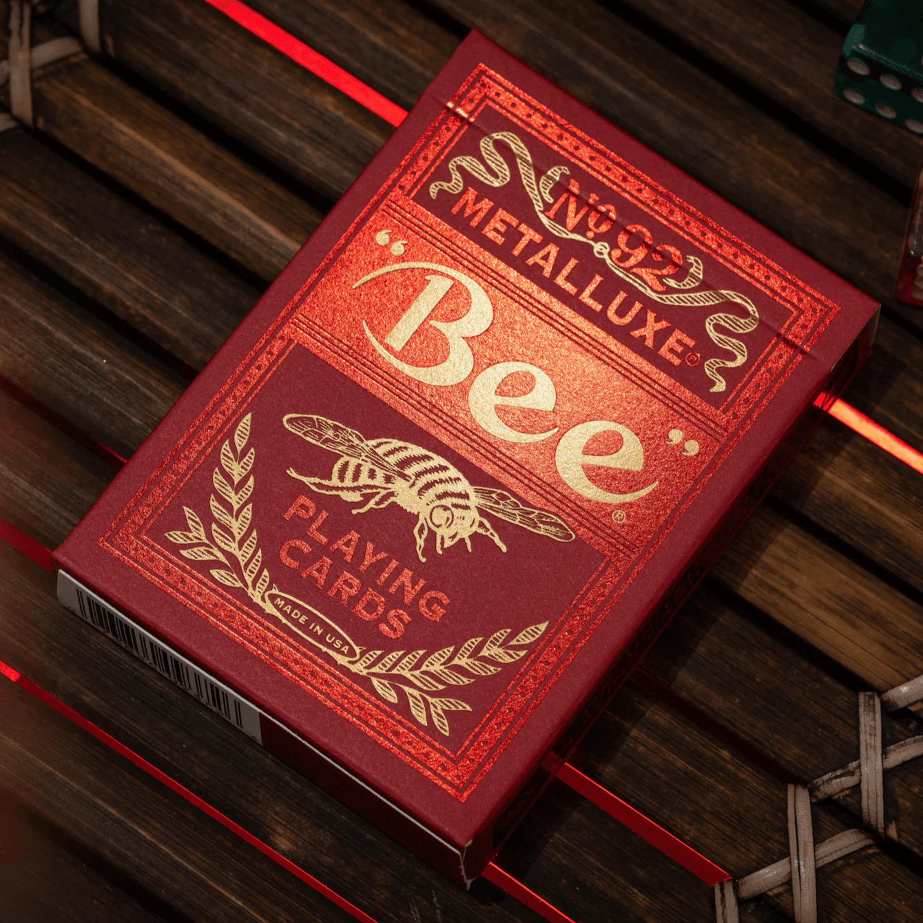 Red and gold playing card box with 'Bee' Metalluxe branding on a wooden surface.