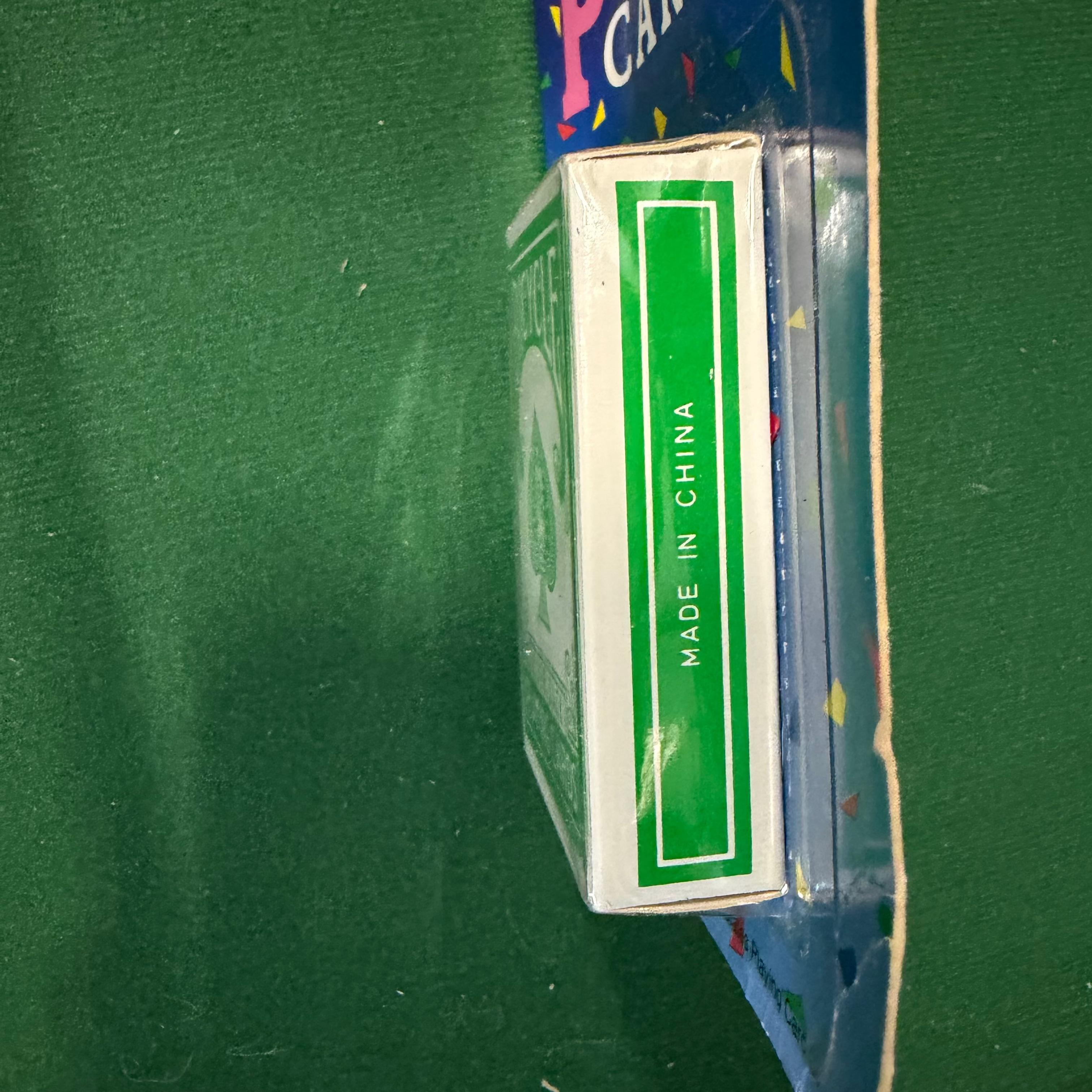 A vintage deck of playing cards in its original blue cardboard packaging, shown on a green felt surface. The side of the box displays a green panel with white text reading 'MADE IN CHINA'.