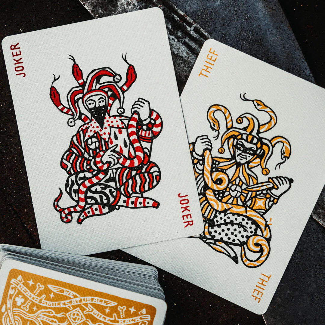 Two playing cards featuring joker and thief designs on a dark surface.