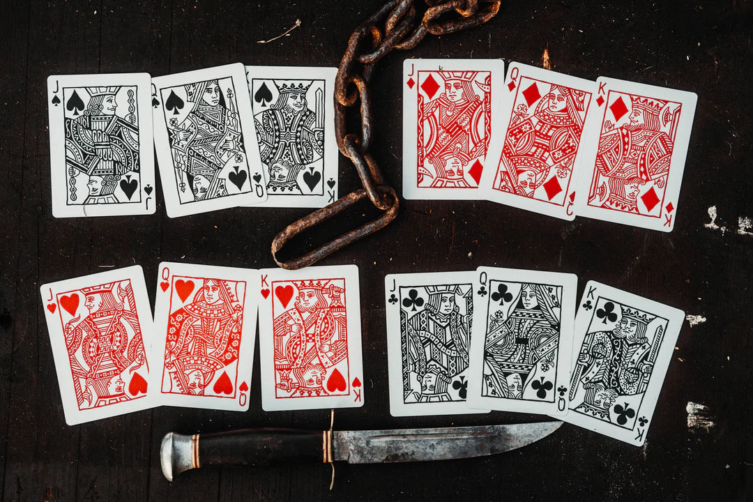 Playing cards with black and red suits on a dark surface with a knife.