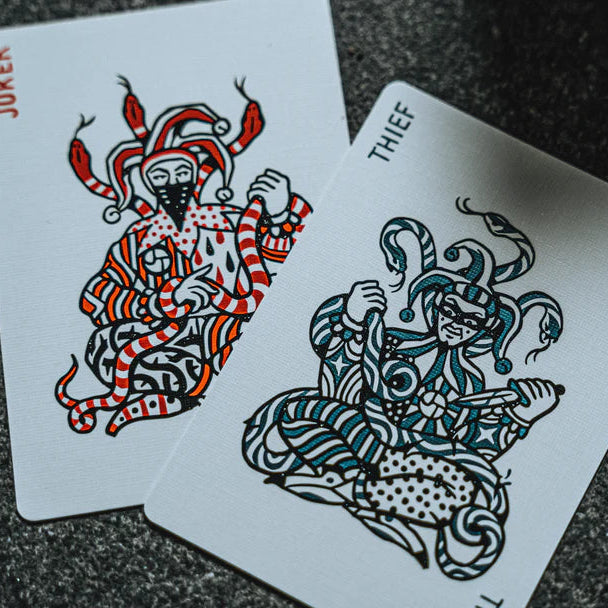 Two playing cards featuring a joker and a thief on a dark textured surface