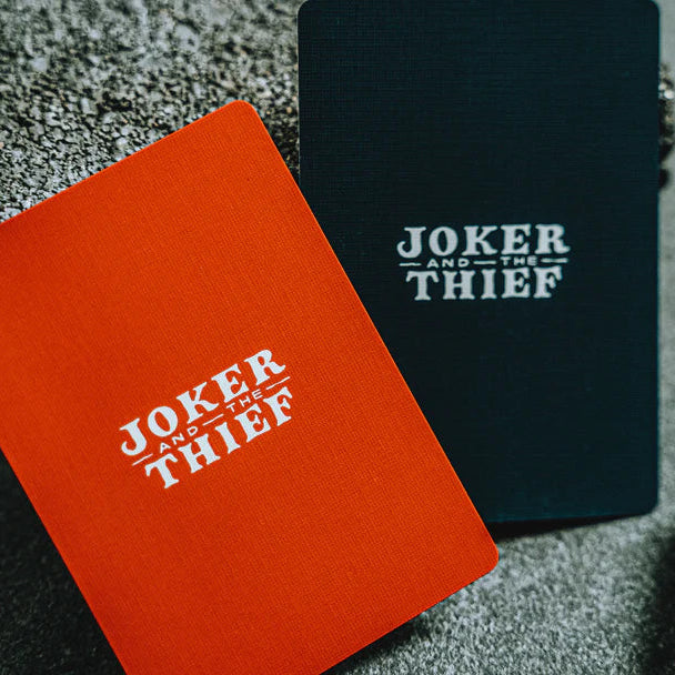 Two playing card decks, one red and one black, with 'Joker and the Thief' branding on a textured surface.