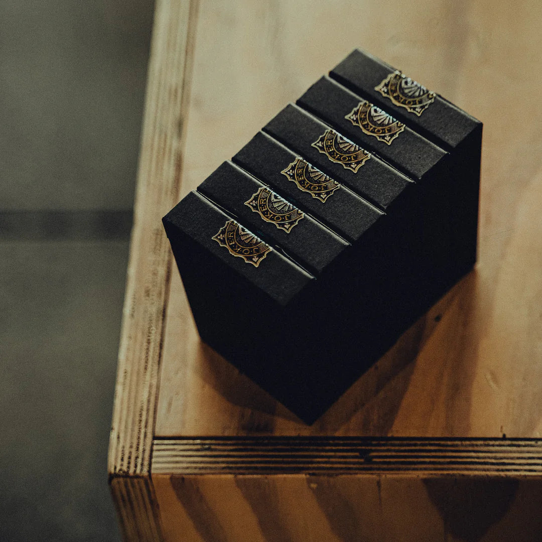 Set of NO BORDERS: Series 2 Playing Cards black boxes with gold accents on a wooden surface