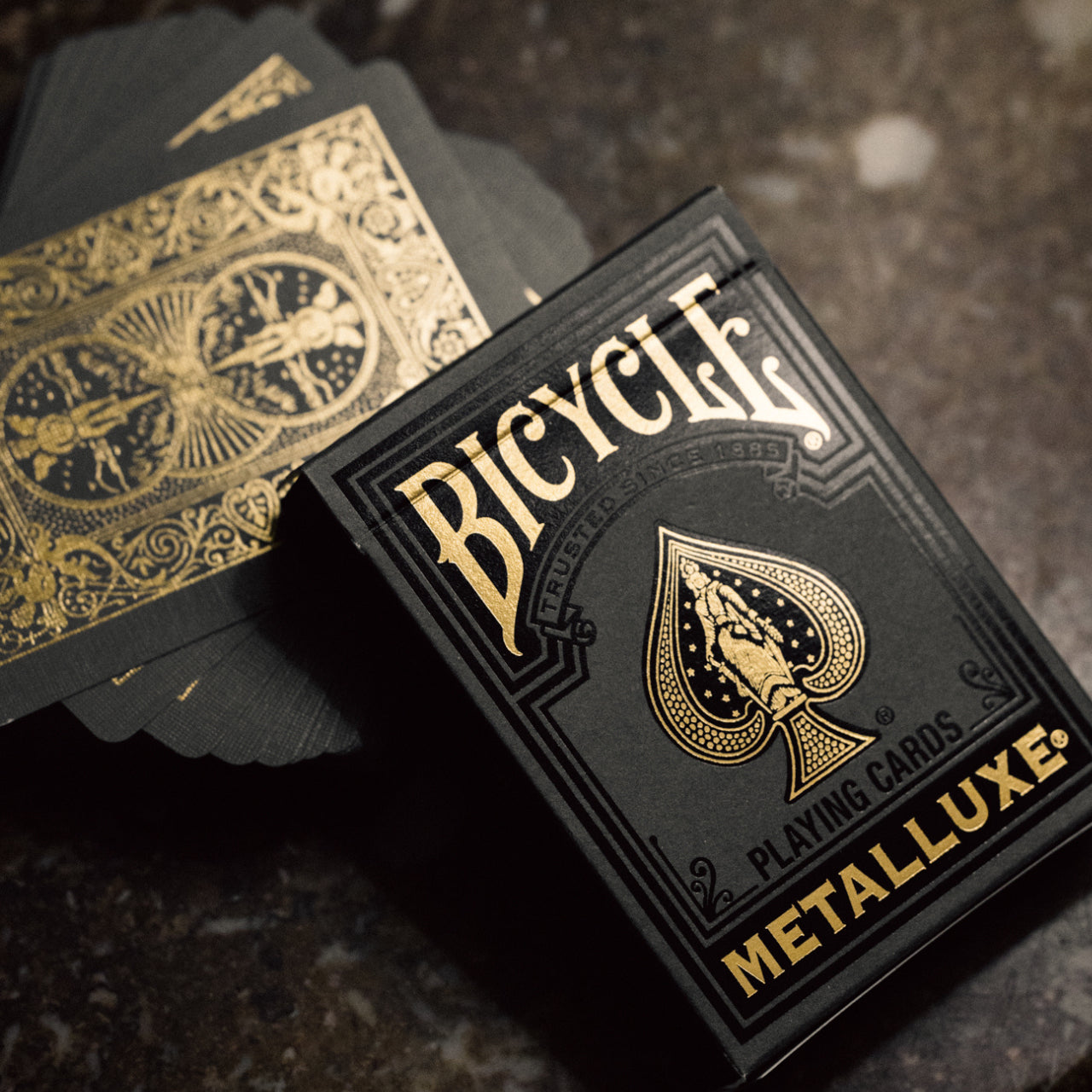 Bicycle Black & Gold Metalluxe playing cards with gold text and design on a dark surface