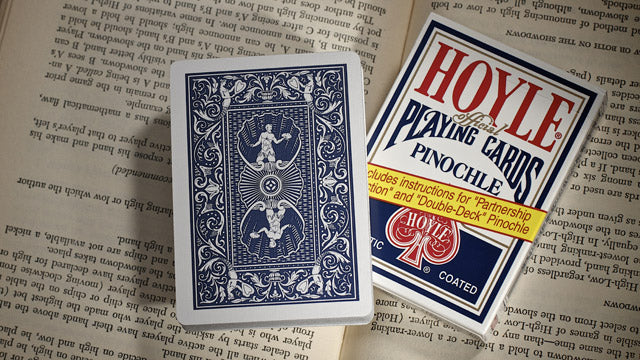 Two decks of playing cards on an open book, one blue and one with 'Hoyle' branding.