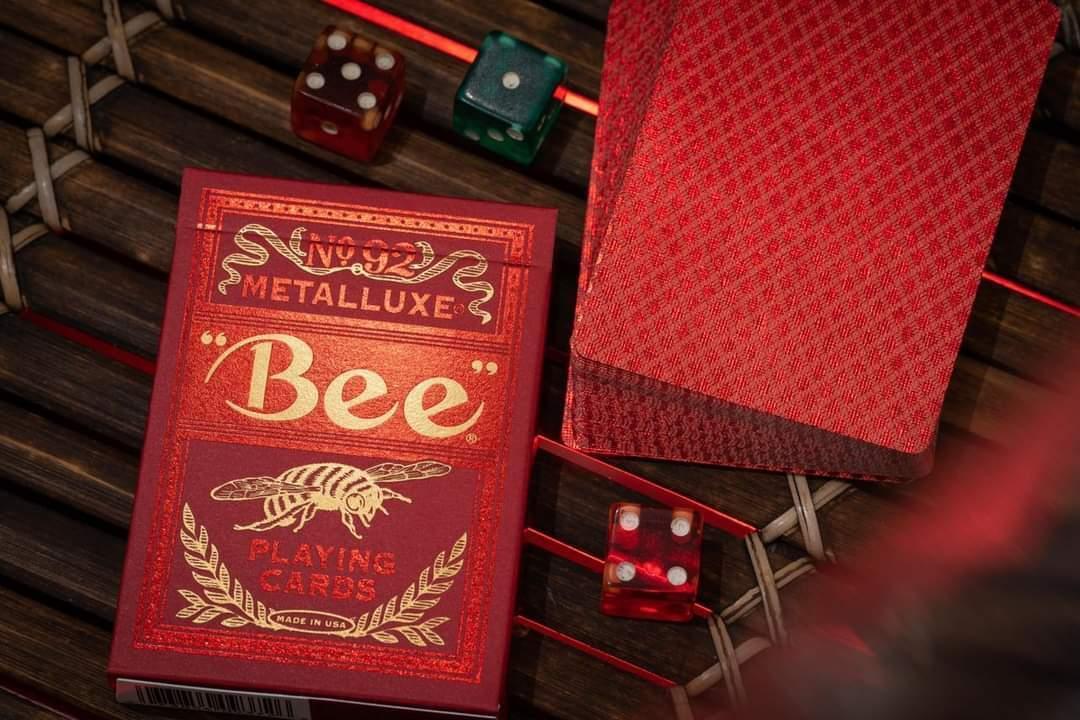 Red 'Bee' Metalluxe playing card box with cards and dice on a wooden surface