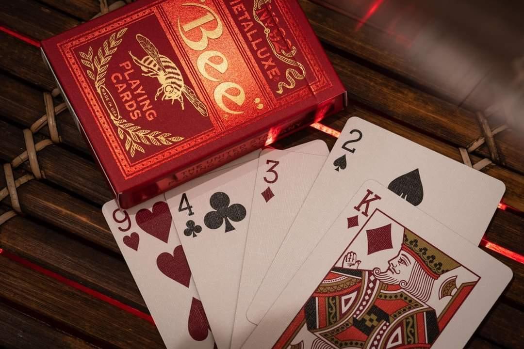 Red Bee Metalluxe playing card box with cards fanned out on a wooden surface