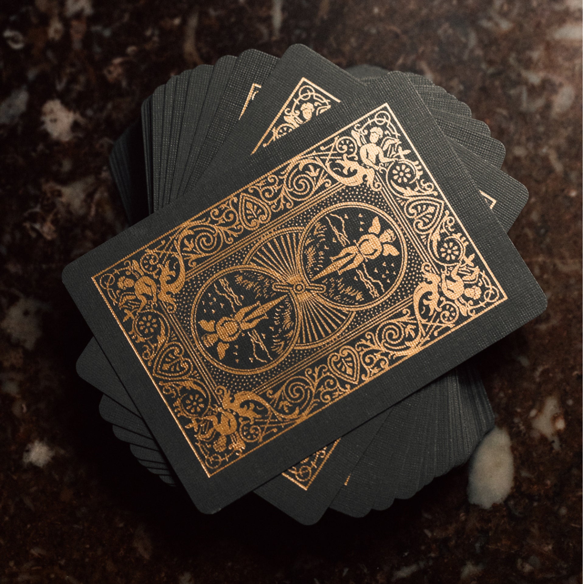 Bicycle Black & Rose Gold Metalluxe playing cards with gold designs on a dark textured surface
