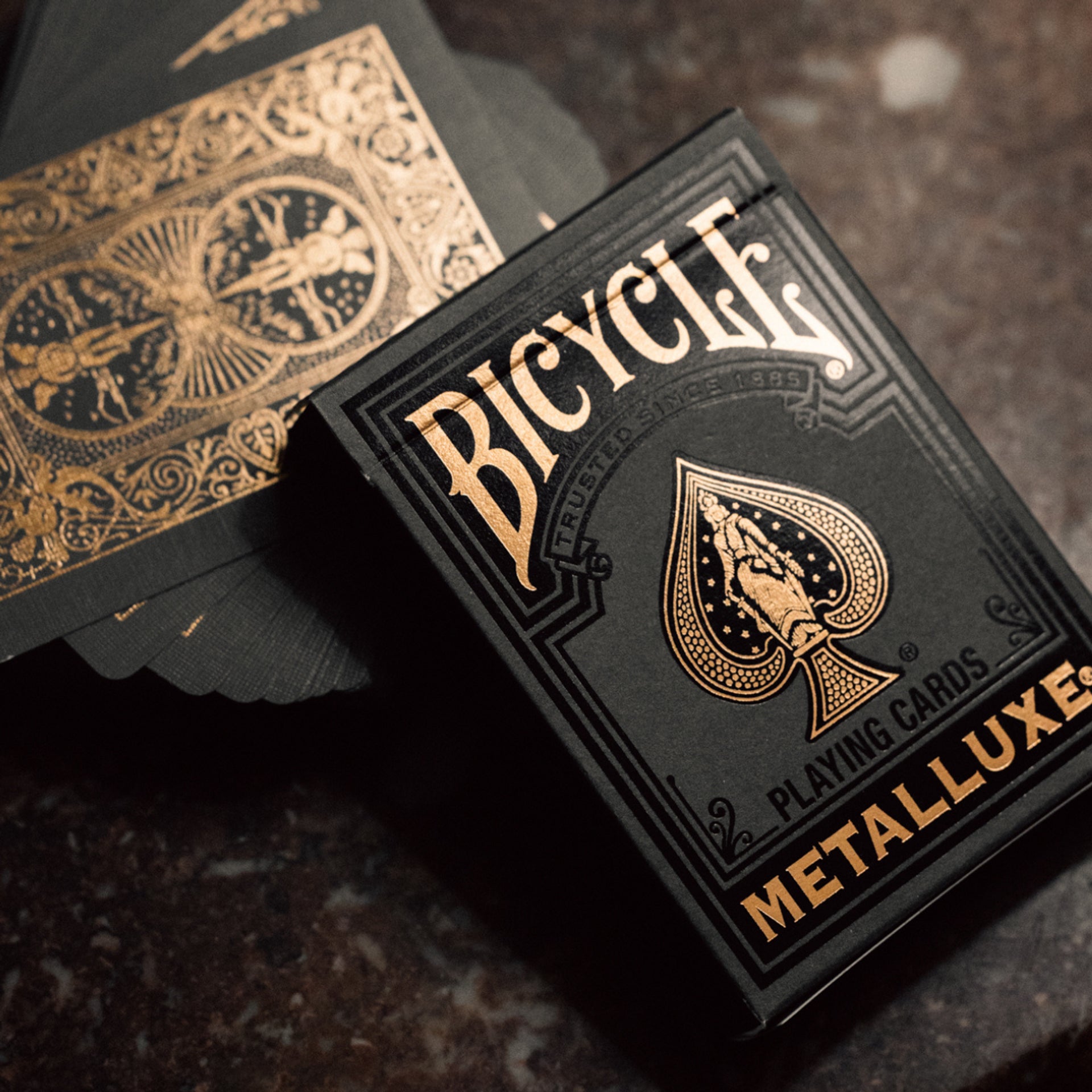 Bicycle Black & Rose Gold Metalluxe playing cards with gold text and design on a dark surface