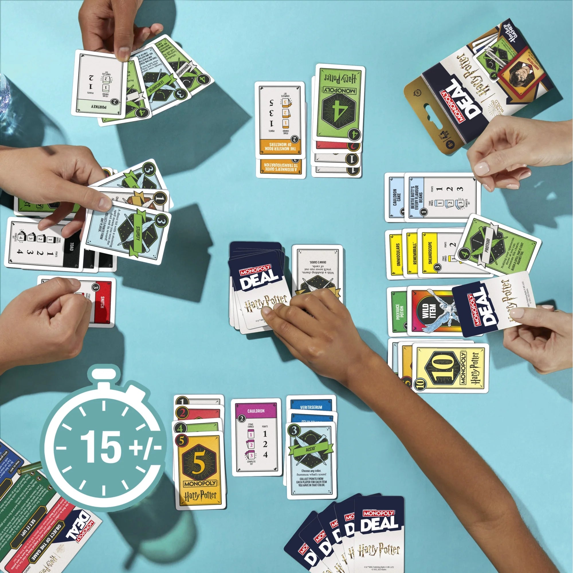 A top-down view of multiple hands holding and playing a Monopoly Deal Harry Potter game on a light blue surface. The scene shows stacks and fanned-out cards from the game, with a large stopwatch graphic in the lower left indicating 15+/- minutes.