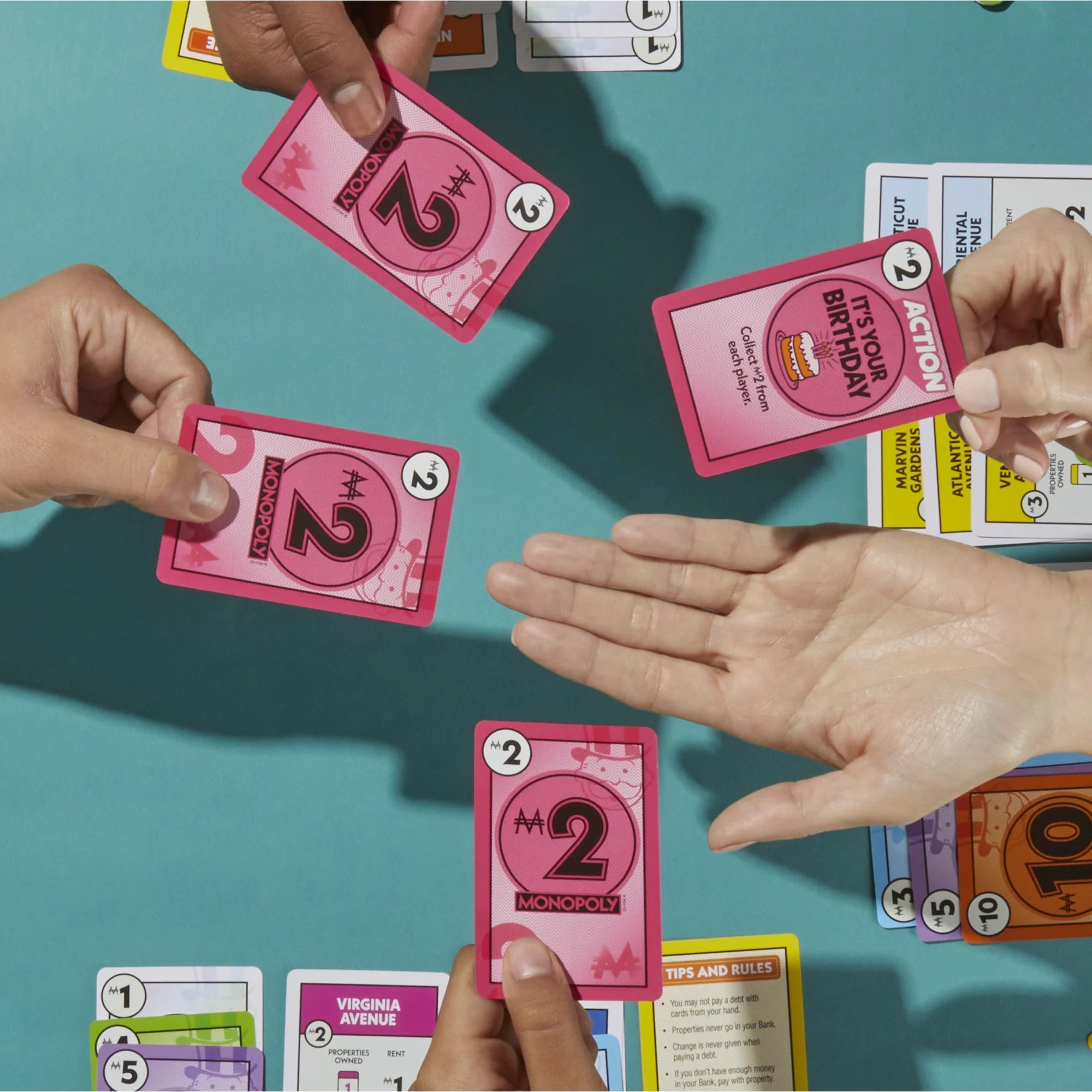 Hands holding pink Monopoly Deal action cards on a blue table
