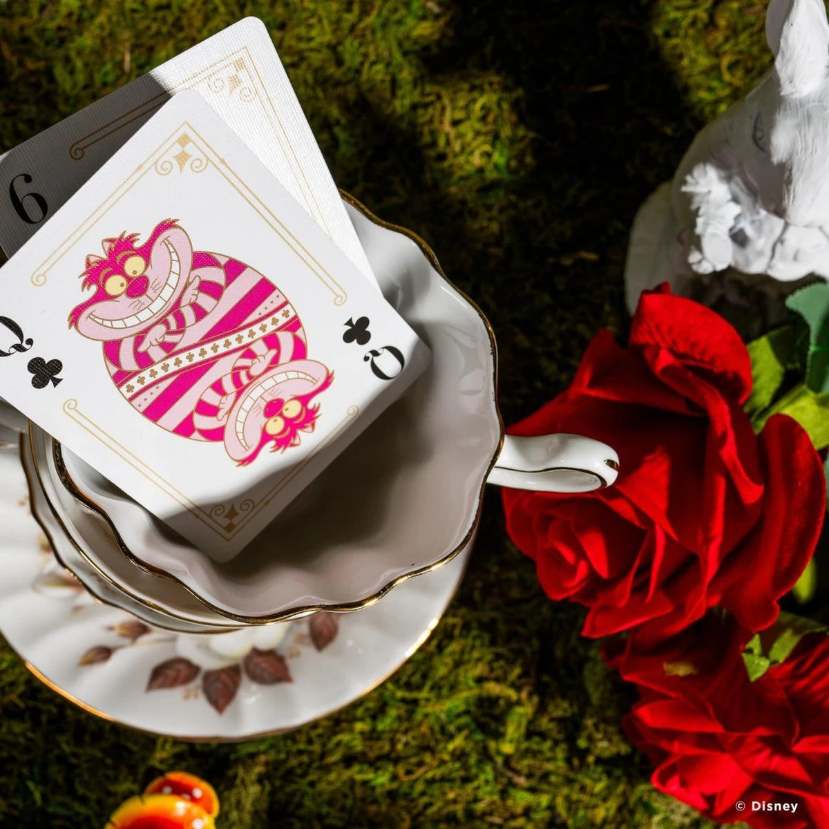 Bicycle Alice in Wonderland Cheshire Cat Queen of Clubs resting on a teacup beside red roses and moss.