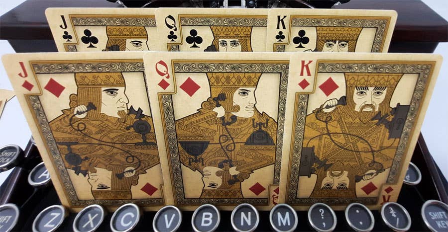 Four playing cards featuring Jack, Queen, King of Clubs from different suits on a typewriter.