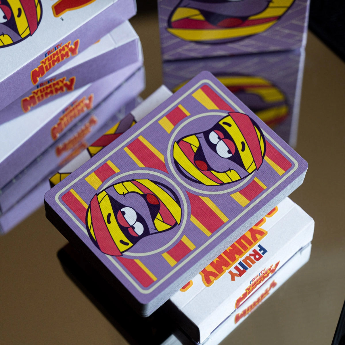 Angled overhead view of a Fruity Yummy Mummy deck displayed across stacked tuck boxes.