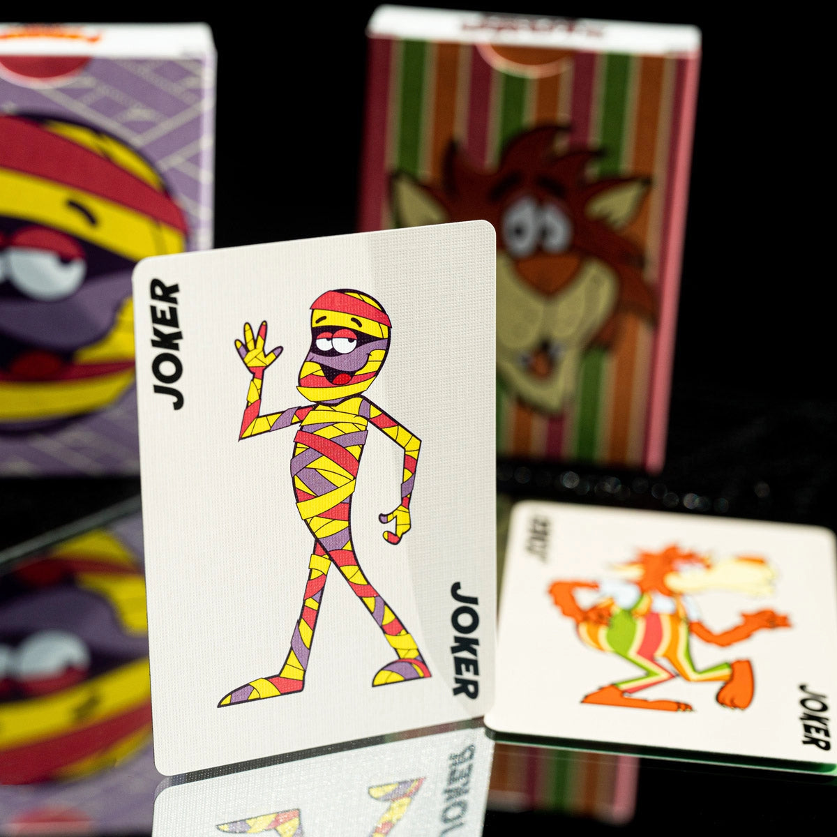 Yummy Mummy Joker standing upright beside the Frute Brute Joker, with tuck boxes behind.