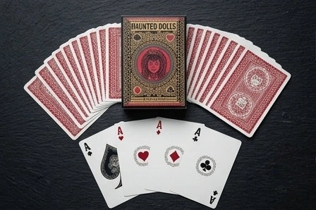 Haunted Dolls Playing Cards tuck box with a fan of red card backs and all four custom Aces on a dark surface