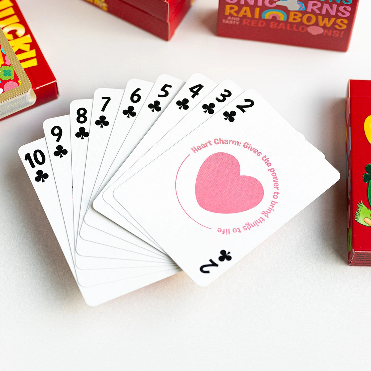 Lucky Charms club number cards fanned from two through ten, with a pink heart charm illustration on the Two of Clubs.