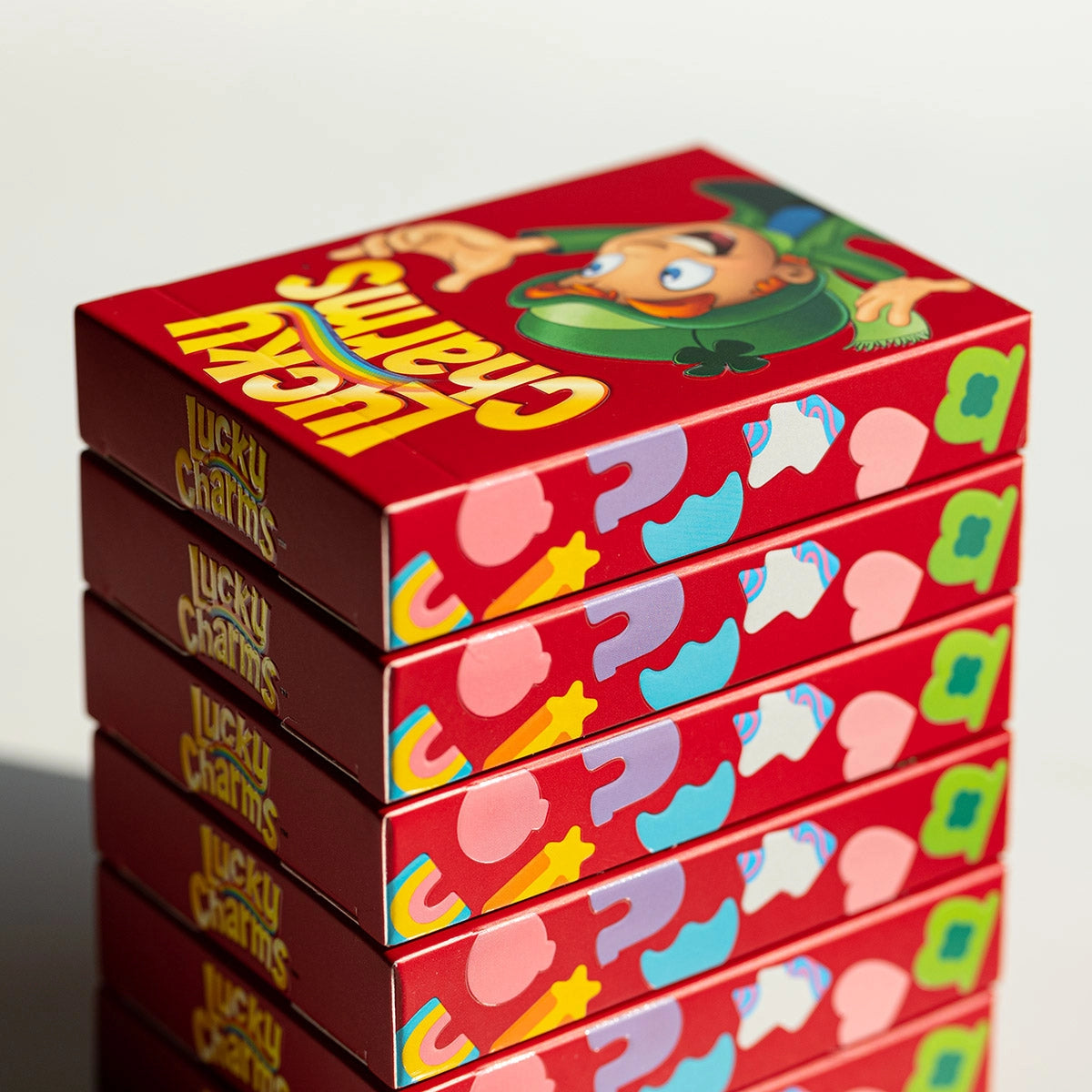 Stacked red Lucky Charms tuck boxes showing marshmallow illustrations along the sides and Lucky on the top box.