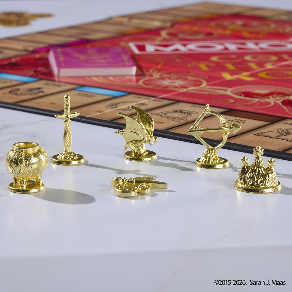 Six golden player tokens from Monopoly A Court of Thorns and Roses on display beside the board.
