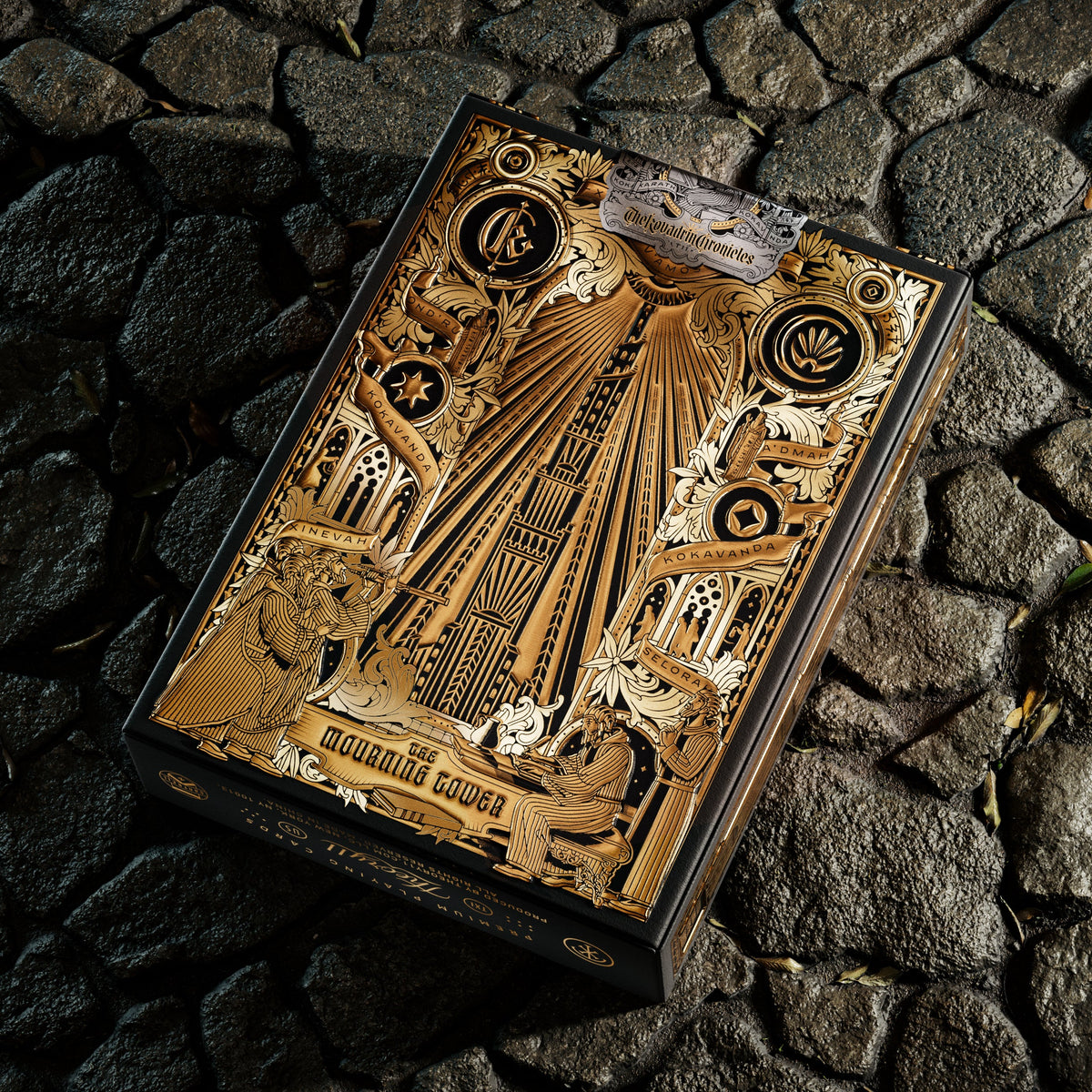 Back of the theory11 Kovadrin tuck box showing the Mourning Tower, decorative symbols, and illustrated figures in gold tones.