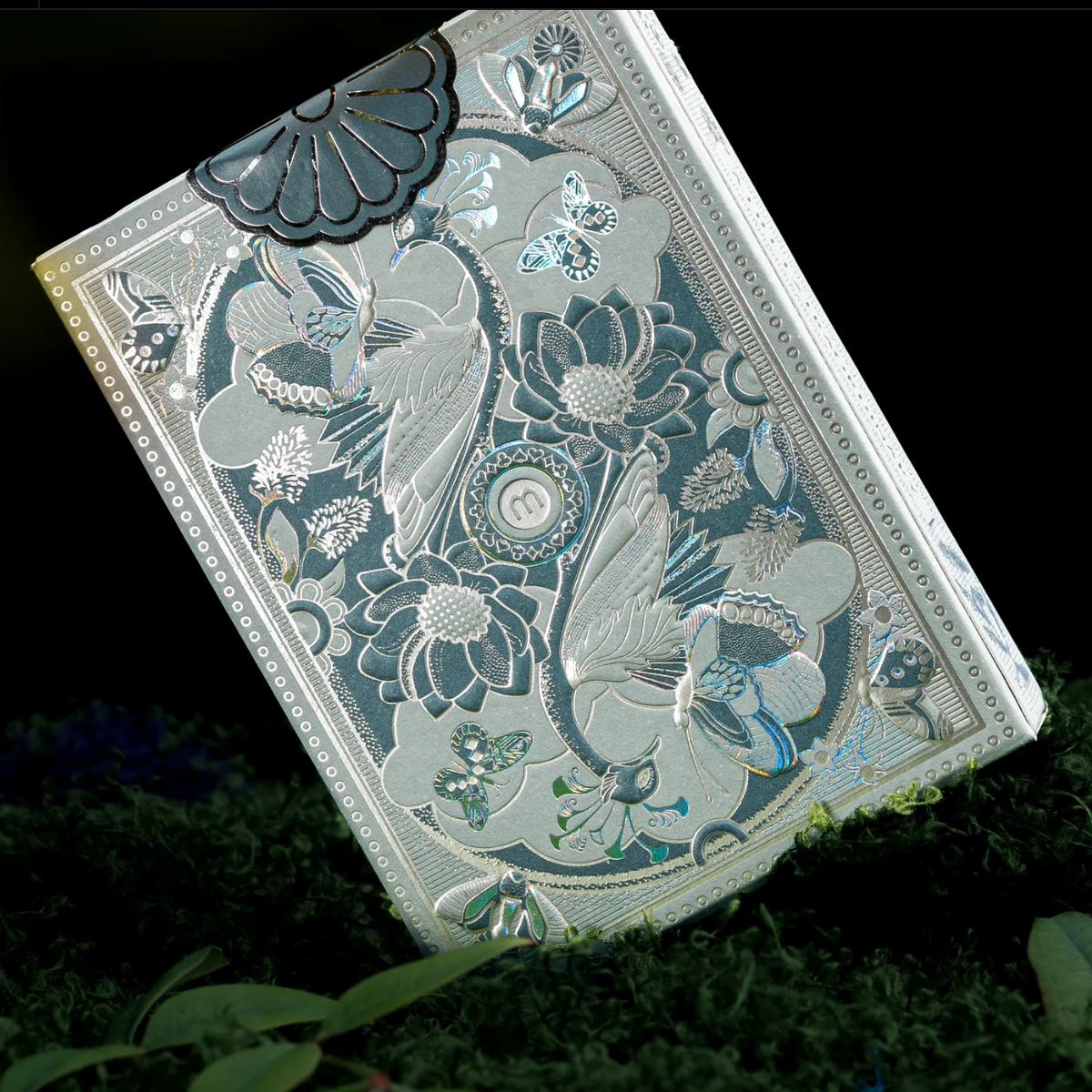 Rear of the Memento Moooi tuck box showing embossed birds, flowers, butterflies, reflective foil, and a floral seal.