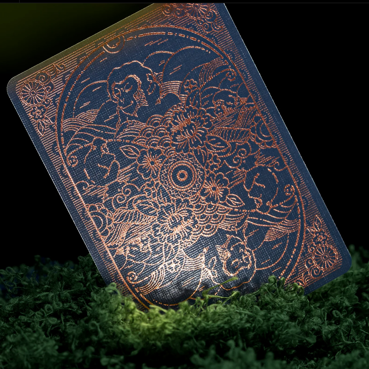 Moooi Tokyo Blue card back with bronze foil macaques, flowers, and mirrored wave patterns, displayed among green moss.
