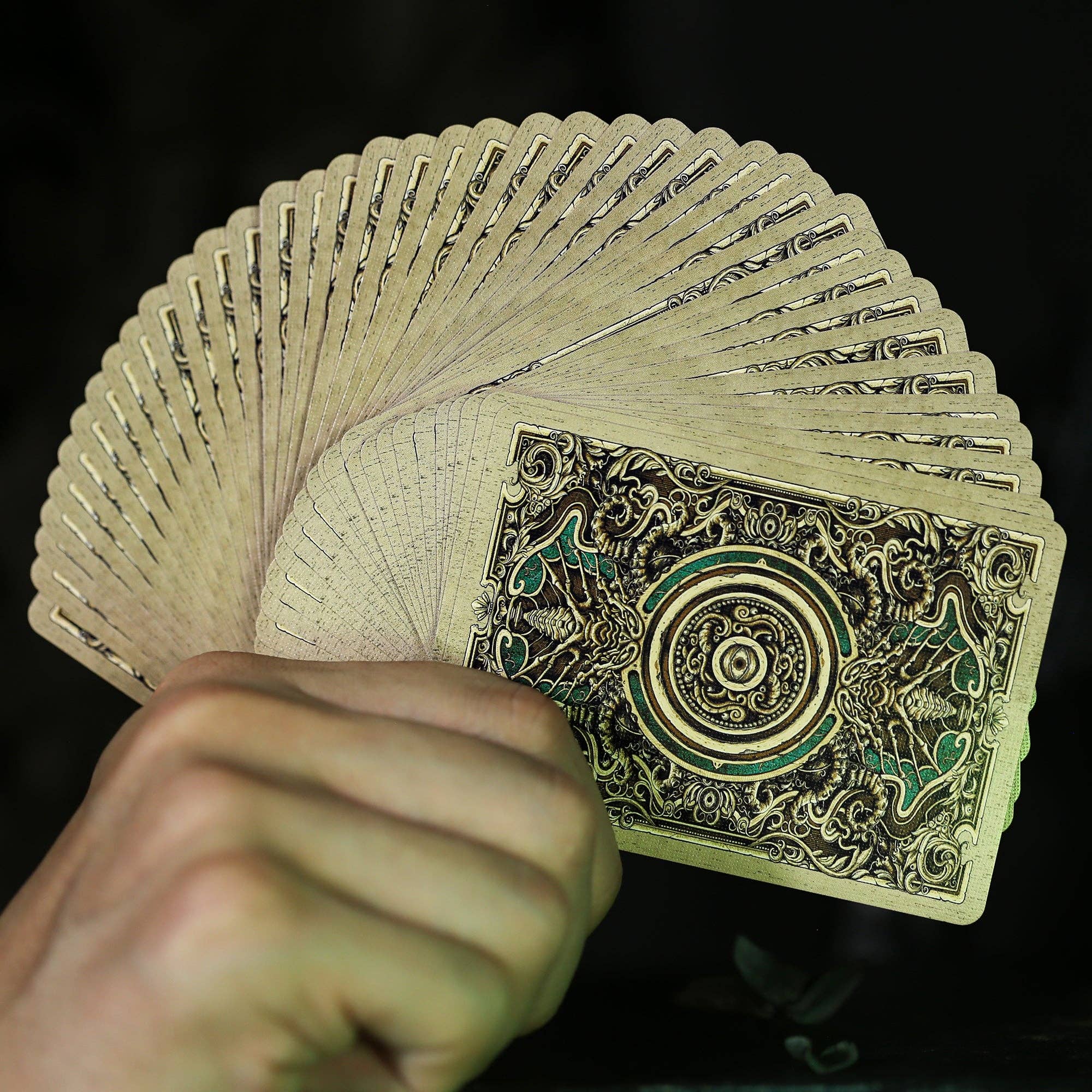 Hand holding a deck of ornate playing cards with intricate designs on a dark background
