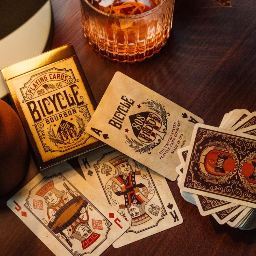 Bicycle Bourbon deck on wooden table with drink, custom Ace of Spades, courts, and back design in view.