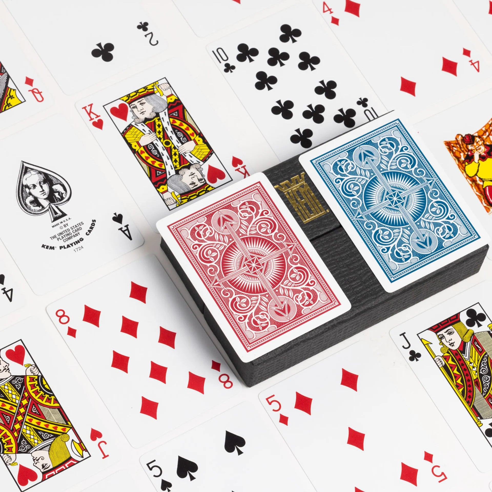 Two decks of KEM playing cards with red and blue backs on a white background with scattered cards.