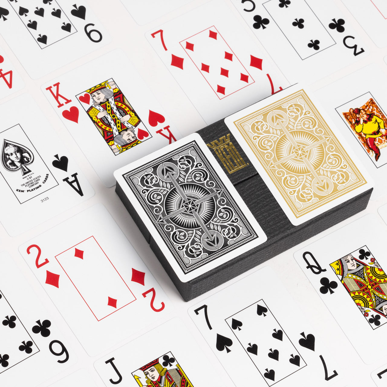 Two KEM Arrow Poker Jumbo Wide Index Playing Card decks, one black and one gold, on a white background with scattered cards.