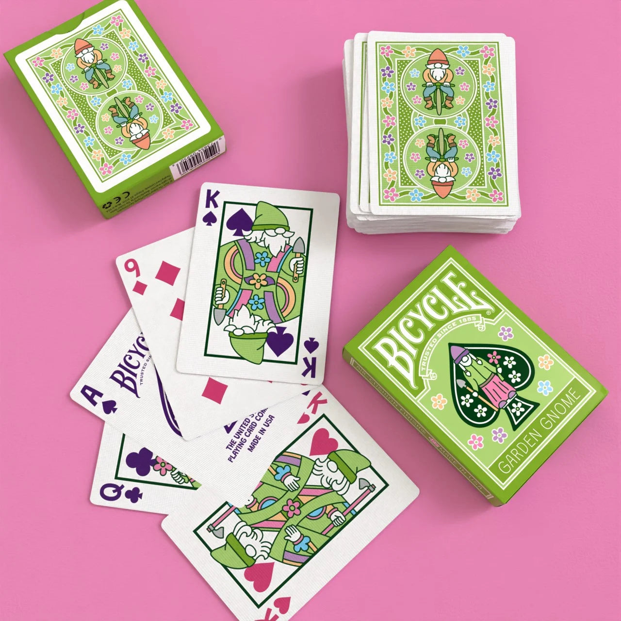 Bicycle Garden Gnome Playing Cards with green tuck boxes, mirrored gnome backs, and custom King and Queen cards on pink background