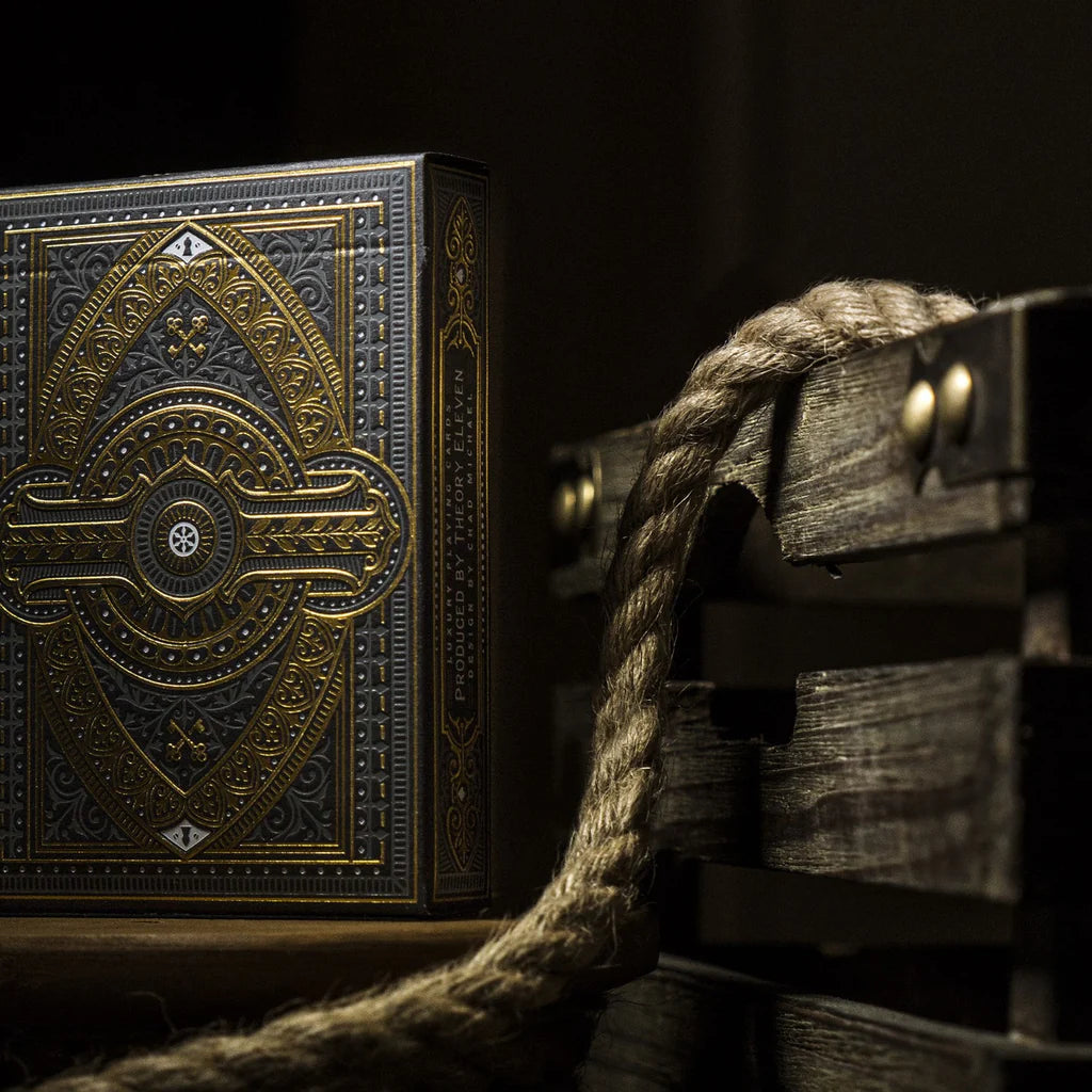 Decorative wooden box with intricate gold patterns next to a wooden crate and rope on a dark background