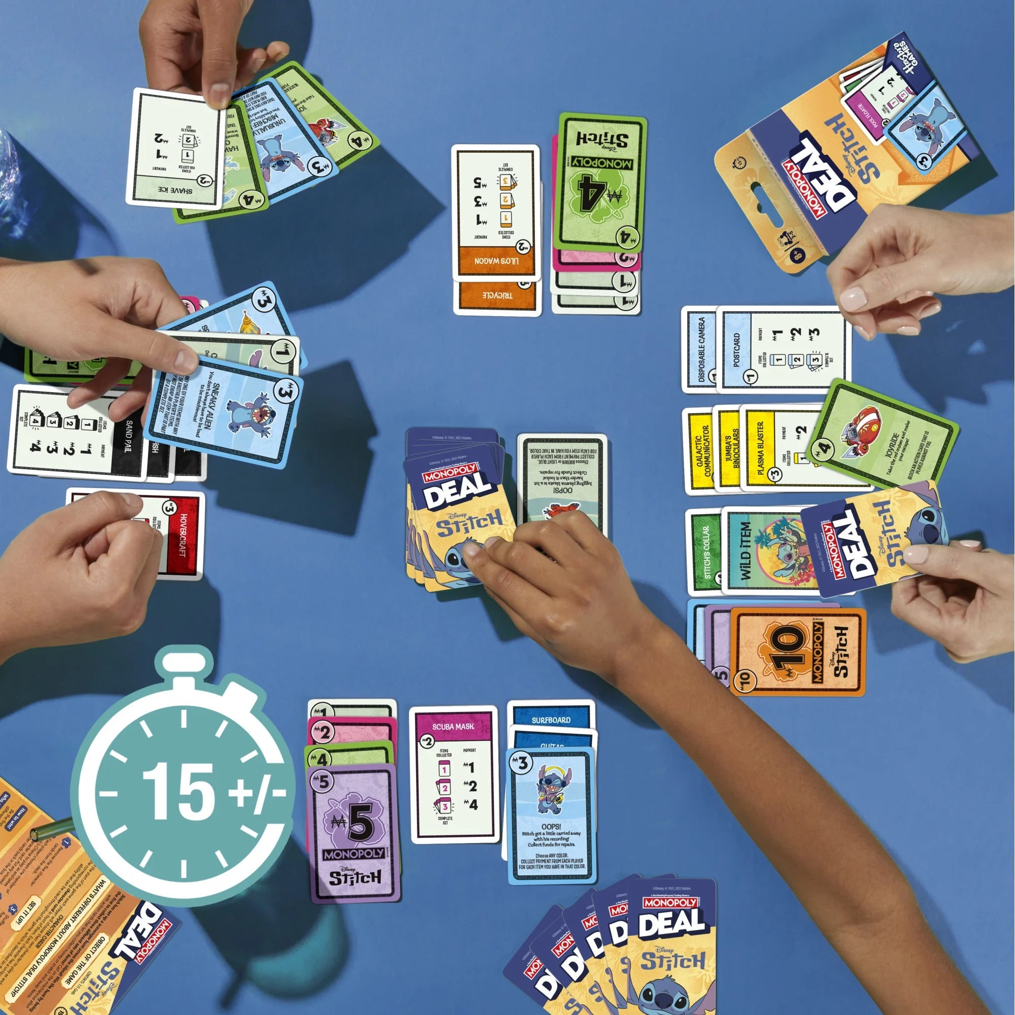 A top-down view of a Monopoly Deal Disney Stitch card game being played by multiple people whose hands and arms are visible around a blue table. Several cards and booster packs are fanned out, including visible branding such as Marvel and Star Wars.