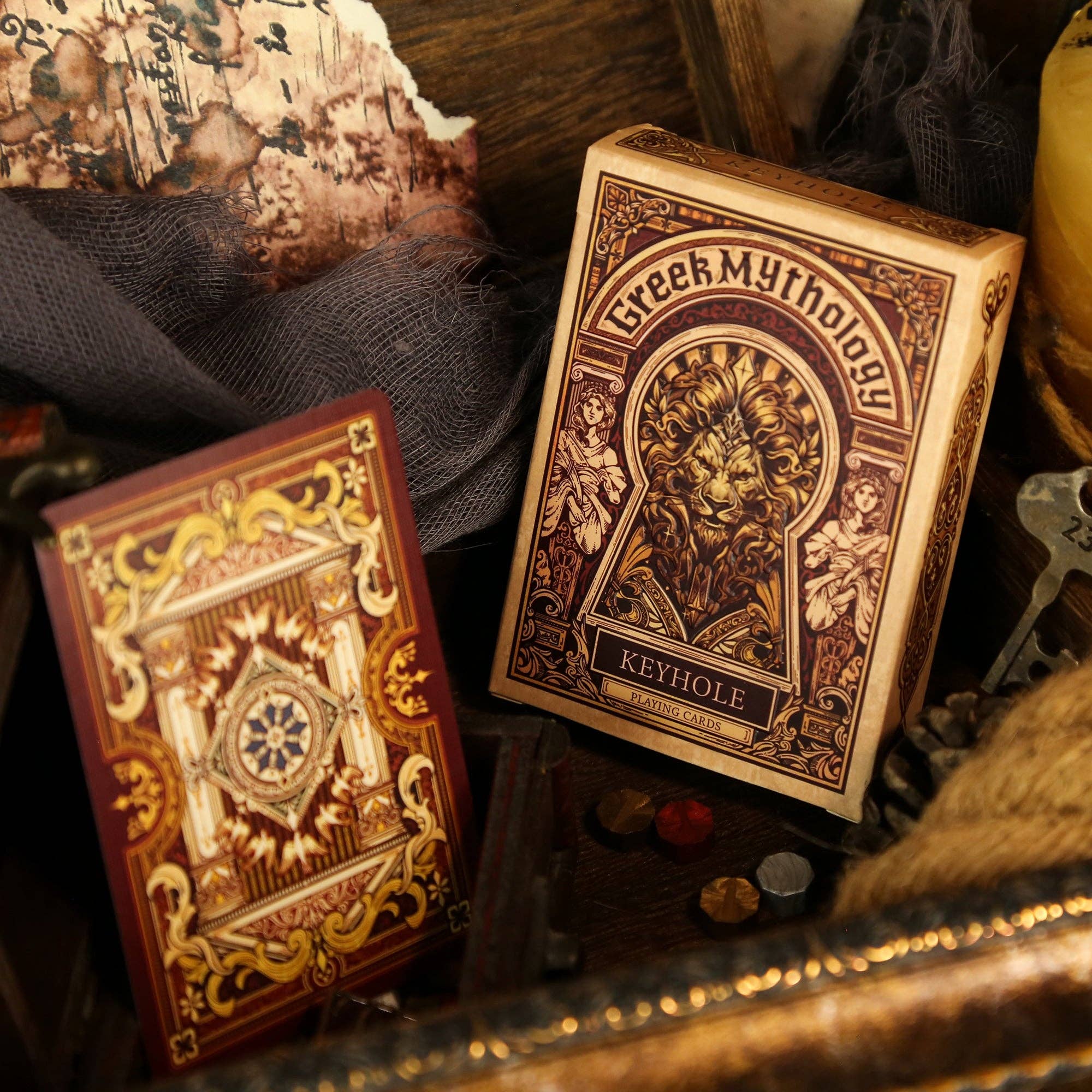 Two Greek Mythology-themed playing card decks on a textured surface with decorative elements.
